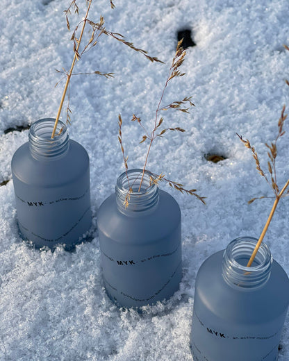 Three blue bottles with plant stems in a snowy landscape